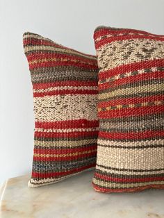 two red and beige striped pillows sitting on top of a marble table