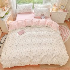 a bed with pink and white comforters in a small room next to a window