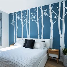 a bedroom with blue walls and white trees painted on the wall behind the headboard