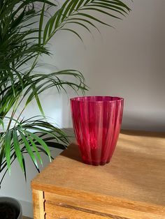 a pink vase sitting on top of a wooden table next to a potted plant