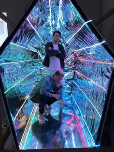 two men standing in front of an art installation with colored lights on the walls and floor