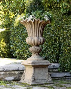 a stone planter sitting in the middle of a walkway next to bushes and trees