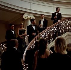 several people in tuxedos are standing on the stairs with lights strung all over them