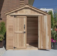 a wooden shed with its doors open and potted plants in the back ground next to it