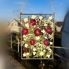 a glass frame with flowers hanging from it's side in front of a house