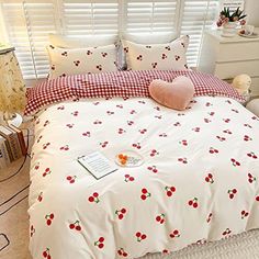 a white bed with cherries on it in a bedroom next to a lamp and window