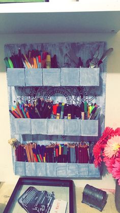 a wooden shelf filled with lots of different colored pens and pencils on top of a table