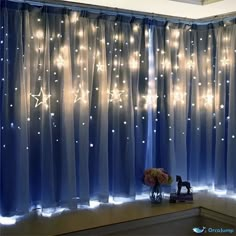 curtains with lights on them are hanging in front of a window, and there is a vase full of flowers next to the curtain