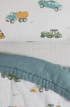 an unmade bed with cars and trucks printed on the sheets, next to a pillow