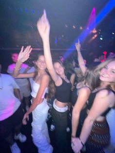 a group of young people dancing at a club or party with their arms in the air