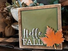 a wooden frame with an orange leaf on it and the words hello fall written in white