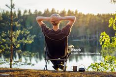 a man sitting in a chair with his back to the camera while looking out over a lake