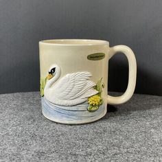 a ceramic mug with a white swan on it's body and yellow flowers in its beak