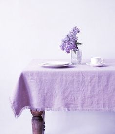 a purple table cloth with a white plate and cup on it next to a vase filled with flowers