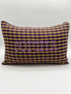 a purple and yellow plaid pillow with an embroidered name on it