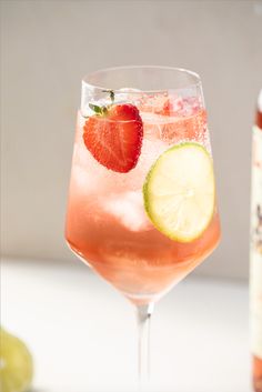 a drink with strawberries and lime in it next to a bottle