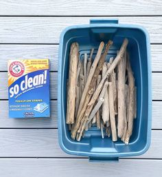 a blue container filled with sticks next to a box of toothpaste on top of a wooden table