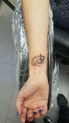 a woman's hand with a small tattoo on her left wrist and the word queen written in cursive font