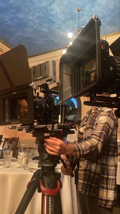 a man standing next to a camera on top of a tripod in front of a table