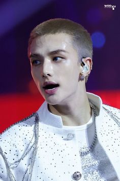 a man with ear piercings on his ears and wearing a white shirt, standing in front of a purple background