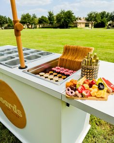 an outdoor buffet with fruit and pastries on the table in front of grass field