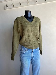 a mannequin wearing a green sweater and blue jeans stands in front of a white wall