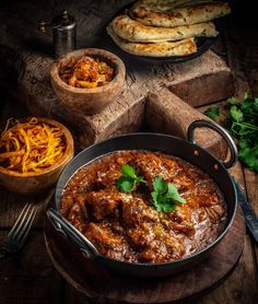 some food is sitting in a pan on a wooden table next to bread and vegetables