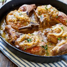 a skillet filled with meat and sauce on top of a wooden table next to a striped napkin