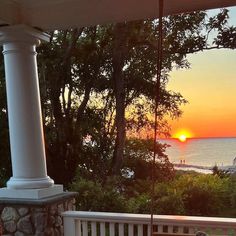 the sun is setting over the ocean and trees in front of a porch with swings