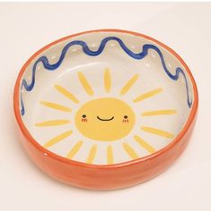 an orange and white bowl with a smiling sun on it's side, against a white background