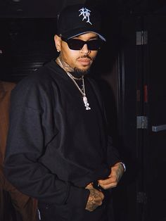 a man wearing sunglasses and a hat standing in front of a door with his hand on his hip