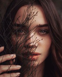 a black and white photo of a woman's face with branches in front of her