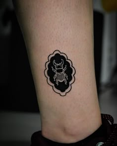 a small tattoo on the ankle of a woman's leg, depicting a beetle