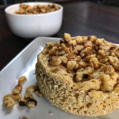 a piece of cake sitting on top of a white plate next to a bowl of nuts