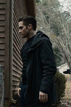 a man standing in front of a house with his hand on the door handle and wearing a black coat