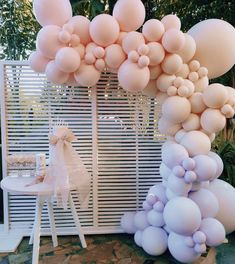 a bunch of balloons that are in the air near a table and chair with a bow on it