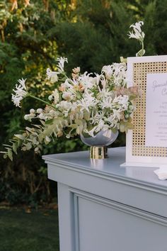 a white and gold wedding stationery with flowers in a silver vase on a table