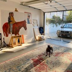 a dog standing in the middle of a room with paintings on the wall and a car parked next to it