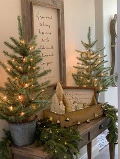 christmas trees are sitting on a table in front of a framed sign and potted plants