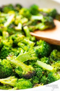 broccoli is being cooked in a white bowl with a wooden spoon on the side