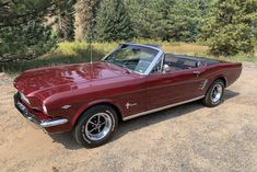 an old red mustang convertible parked in the dirt