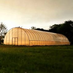 a large green house sitting in the middle of a lush green field next to trees