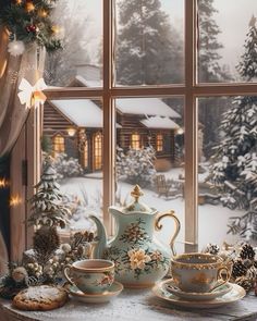 a tea set sitting on top of a table next to a window covered in snow