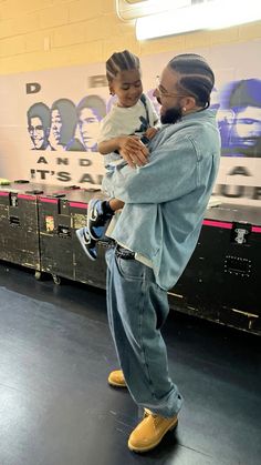 a man holding a child in his arms while standing next to lockers with posters on the wall behind him