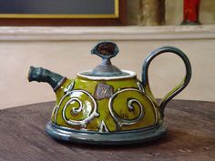 a green teapot sitting on top of a wooden table next to a framed painting