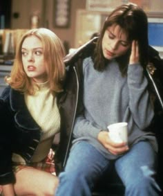 two young women sitting next to each other on a bench, one holding a coffee cup