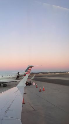 an airplane is sitting on the runway at sunset or dawn, with orange cones around it