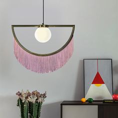 a room with a table, vase and pictures on the wall next to it is a lamp that has pink fringes hanging from it