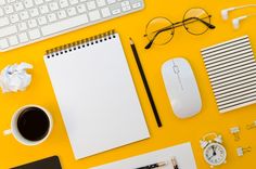 an overhead view of office supplies on a yellow background with a keyboard, mouse and glasses