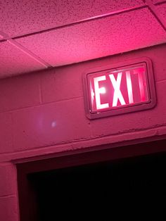 an exit sign is lit up in pink light on a brick wall above a doorway